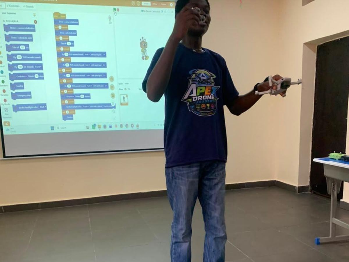 Drone Club session: instructor holding a drone with block-coding projected behind