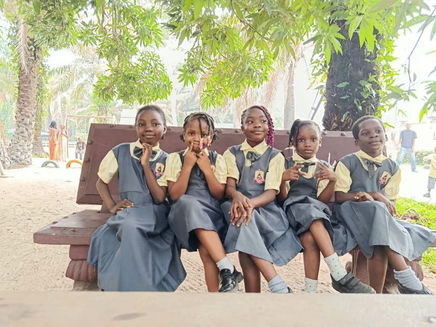 Five pupils sitting together on a park bench under the trees